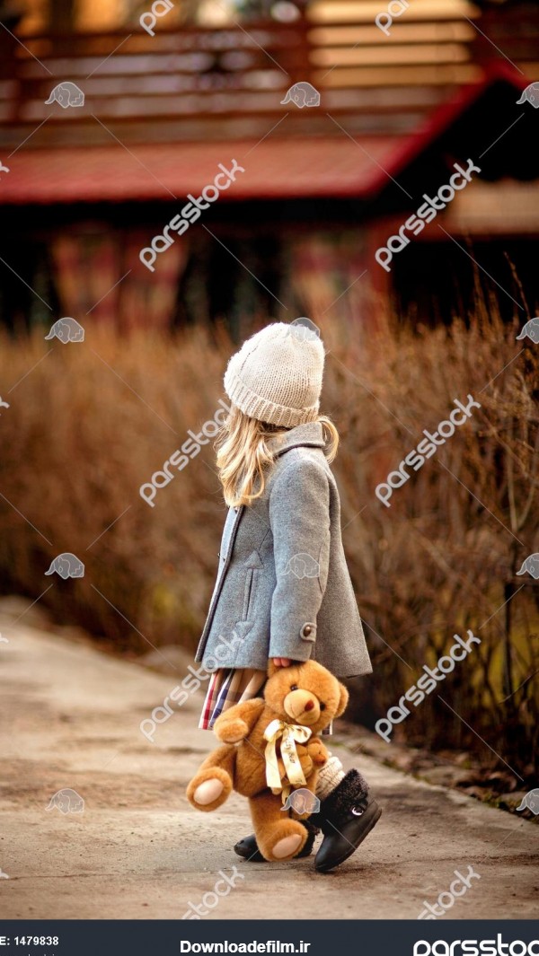دختر کوچکی که با یک خرس عروسکی در دستش در باغ قدم می زند 1479838