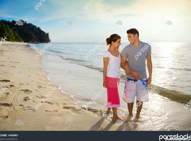 زوج خوشبختی که در امتداد یک ساحل غروب خورشید عاشقانه قدم می زنند ...