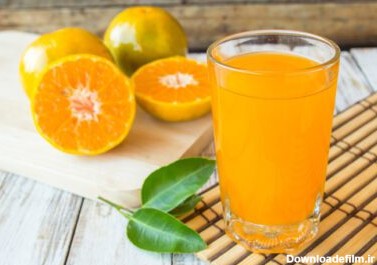 دانلود عکس لیوان آب پرتقال تازه پرس شده با تکه تکه پرتقال روی
