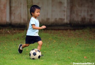 دانلود عکس پسر آسیایی در حال بازی فوتبال در پارک بچه دریبل زدن توپ