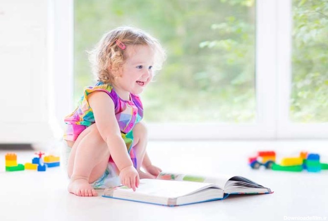 دانلود تصویر با کیفیت دختر بچه خندان در حال نگاه کردن به کتاب