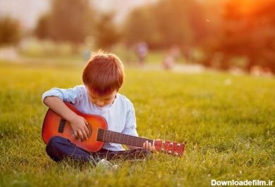 دانلود پسر شایان ستایش با گیتار ، که در غروب آفتاب روی چمن ها نشسته است