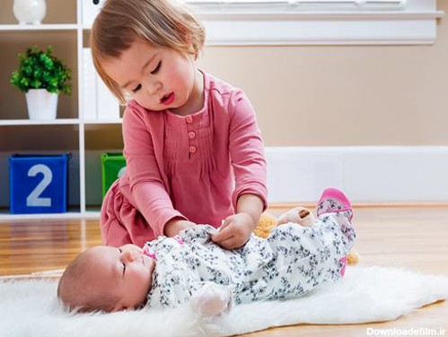 تصویر با کیفیت از دختر کوچولو در حال پوشاندن پیراهن به نوزاد
