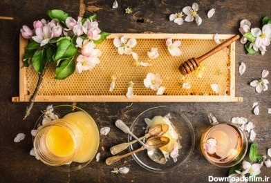 دانلود لانه زنبوری با گلدان چوبی و شکوفه تازه ، کوزه با عسل و بشقاب با قاشقهای پرنعمت در زمینه تیره روستایی ، نمای بالا