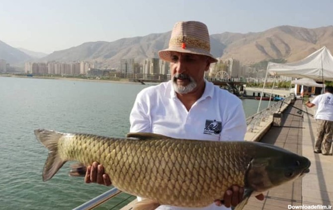 مردی در کنار دریاچه با ماهی بزرگی در دستش