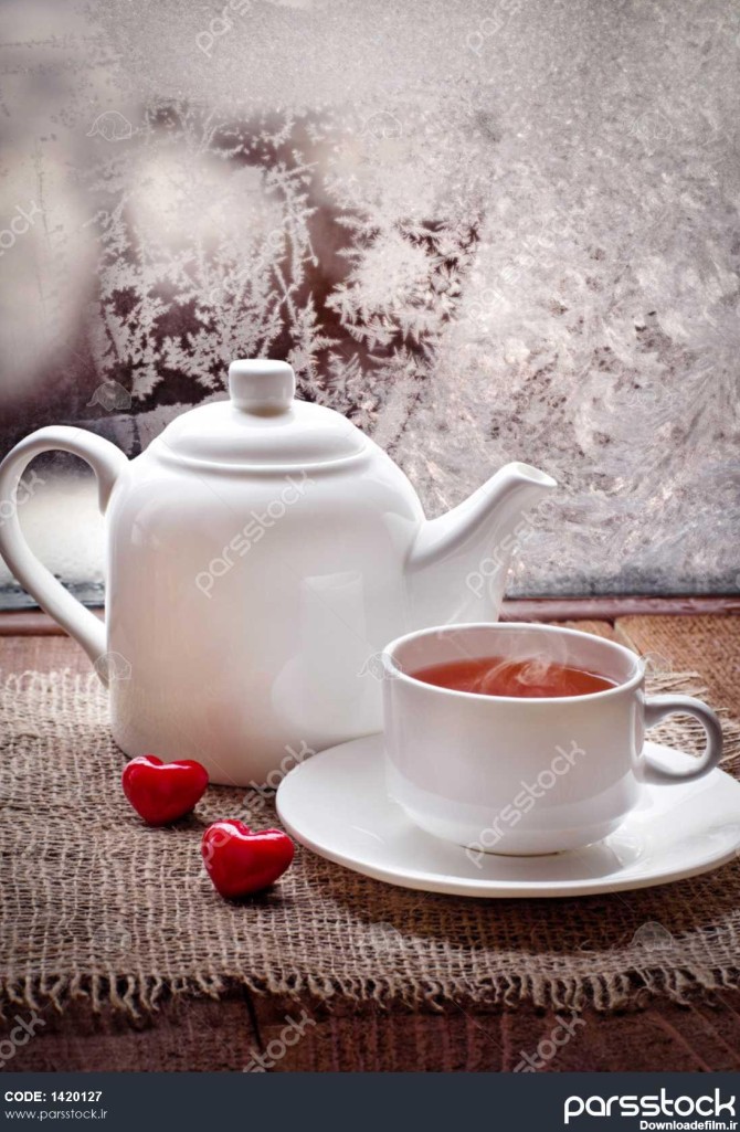 فنجان چای و قوری با قلب قرمز بر روی میز قدیمی چوبی در روز یخ ...