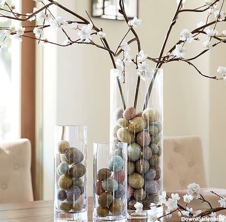 گلدان استوانه ای شیشه ای که در آن شاخه شکوفه مصنوعی و تخم مرغ های تزئینی قرار داده شده است