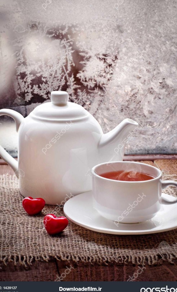 فنجان چای و قوری با قلب قرمز بر روی میز قدیمی چوبی در روز یخ زده ...