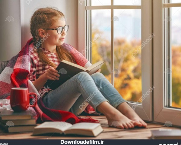 دختر بچه ناز نشسته در پنجره و خواندن یک کتاب در اتاق در منزل طبیعت ...