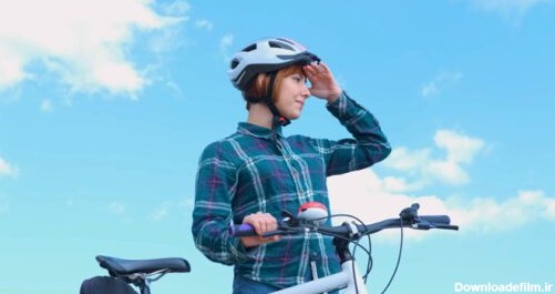 دانلود عکس زن جوان دوچرخه سوار با کلاه ایمنی در روز آفتابی تابستان