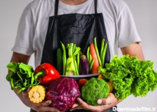 دانلود عکس مردی که پیش بند پوشیده است و سبزیجات مختلف را در هر دو دست گرفته است
