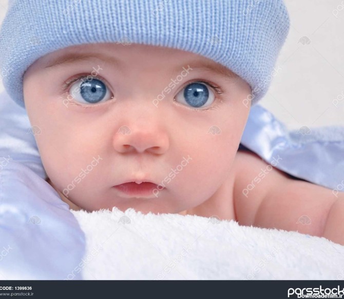 یک بچه کوچک با چشم آبی با یک کلاه خیره شده است کودک روی پتو است ...