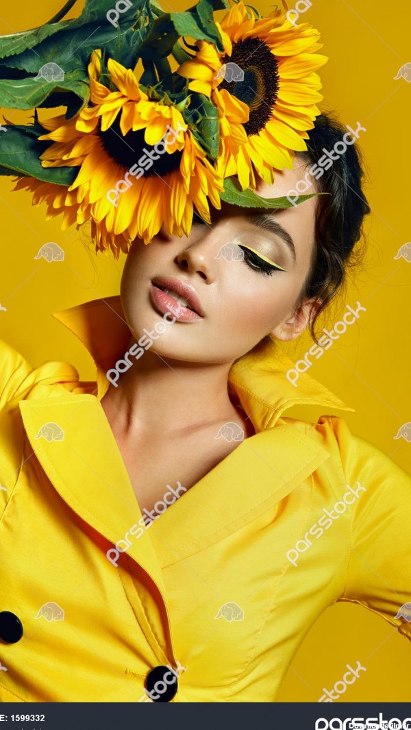 دختری با لباس زرد یک دسته گل آفتابگردان زرد در دستانش نگه داشته ...